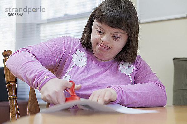 Mädchen mit Down-Syndrom schneidet ein Papier mit einer Schere