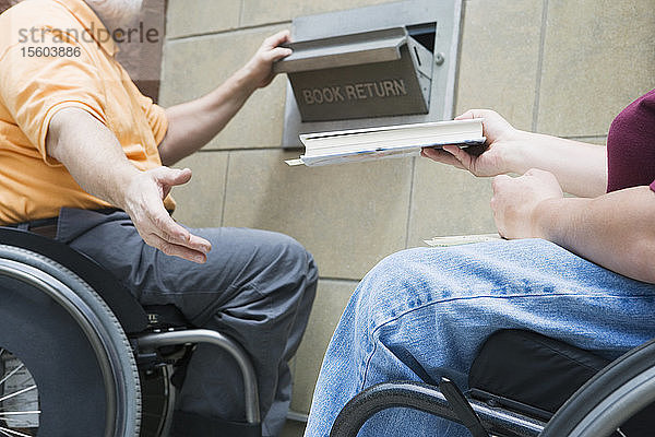 Ehepaar im Rollstuhl mit Muskeldystrophie gibt ein Buch in einer Bibliothek zurück