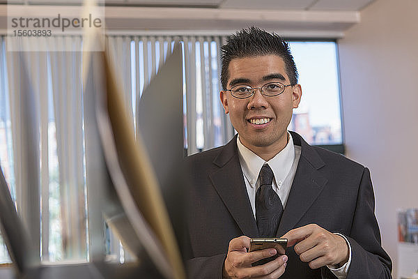 Asiatischer Mann mit Autismus arbeitet in einem Büro mit seinem Telefon