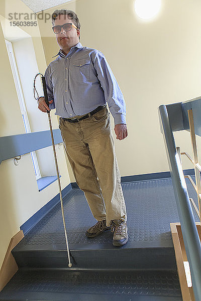 Mann mit angeborener Blindheit benutzt seinen Stock  um eine Treppe hinunterzugehen