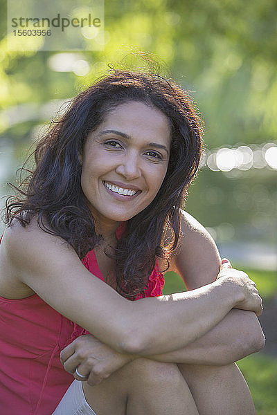Porträt einer glücklichen hispanischen Frau  die in einem Park sitzt