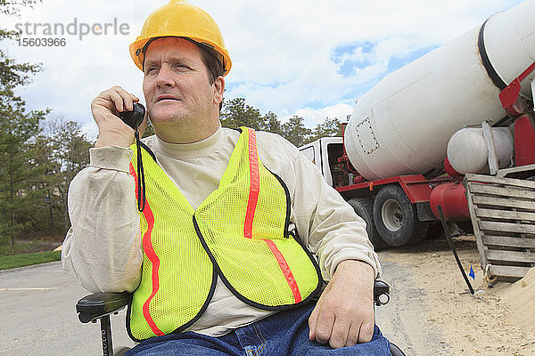 Bauleiter mit Querschnittslähmung am Walkie-Talkie mit Betonmischwagen