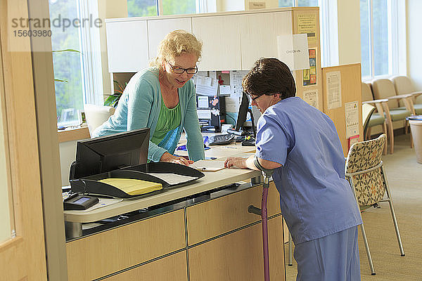 Krankenschwester mit Cerebralparese fragt bei der Verwaltung nach den Unterlagen eines Patienten in einer Klinik