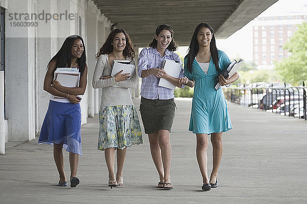 Vier Mädchen im Teenageralter  die Bücher in der Hand halten und auf dem Schulcampus abhängen