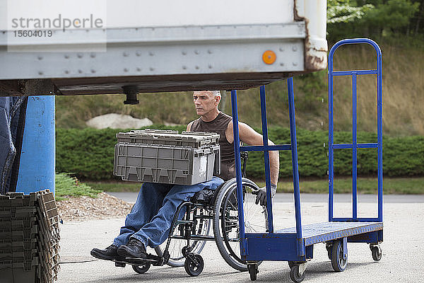 Laderampenarbeiter mit Rückenmarksverletzung im Rollstuhl beim Bewegen von gestapelten Inventartabletts