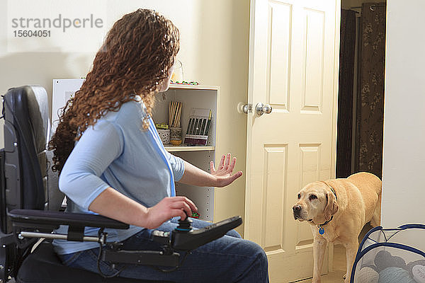 Eine Frau mit Muskeldystrophie in ihrem Rollstuhl fordert ihren Diensthund auf  zu bleiben