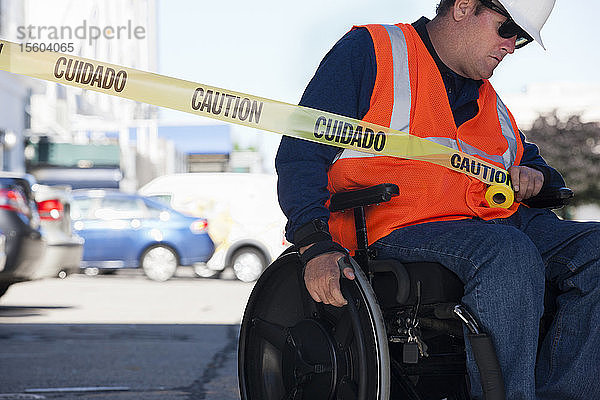 Ein Techniker im Rollstuhl zieht ein Absperrband über die Straße