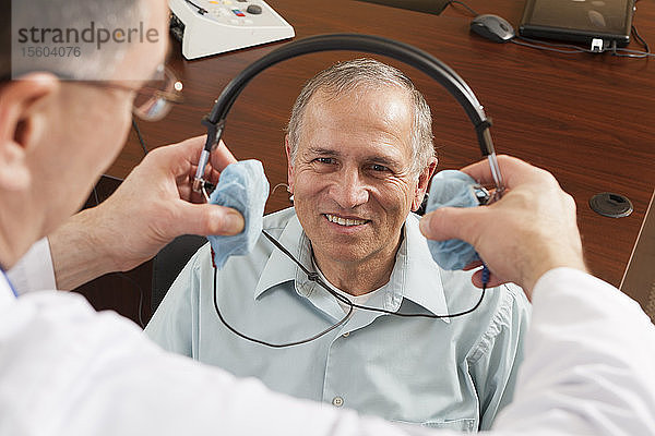 Audiologe setzt dem Patienten für die audiometrische Untersuchung ein Headset auf