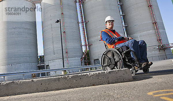 Gebäudetechniker im Rollstuhl bei der Inspektion von Lagertanks für Schüttgut im Freien