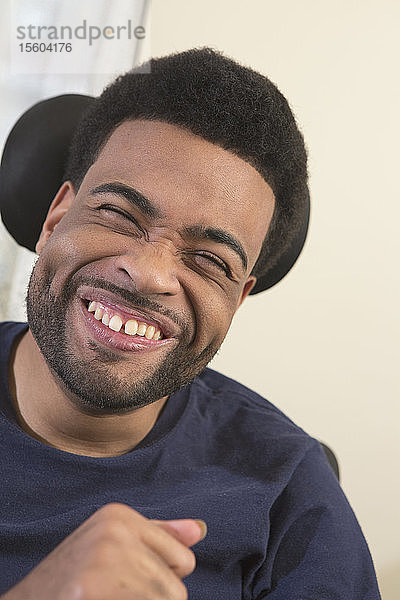 Porträt eines glücklichen afroamerikanischen Mannes mit zerebraler Lähmung  der zu Hause im Rollstuhl lächelt