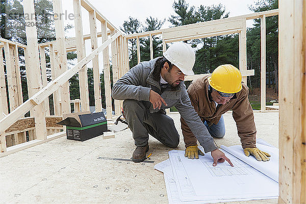 Ein Bauleiter bespricht mit einem Zimmermann den Bauplan eines Hauses