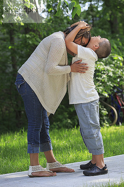 Hispanischer Junge mit Autismus umarmt seine Mutter im Park