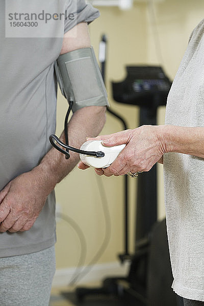 Frau prüft den Blutdruck eines Mannes im Fitnessstudio.