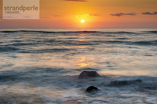 Untergehende Sonne über dem Horizont des Ozeans mit sanft rollenden Wellen; Kauai  Hawaii  Vereinigte Staaten von Amerika