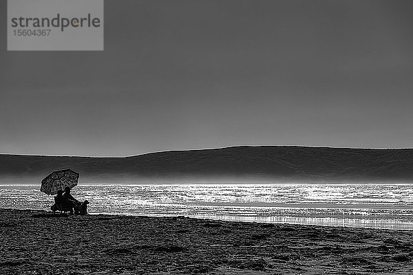 Schwarz-Weiß-Bild eines Paares  das am Dillon Beach am Rande des Wassers sitzt und auf den Ozean hinausschaut; Kalifornien  Vereinigte Staaten von Amerika