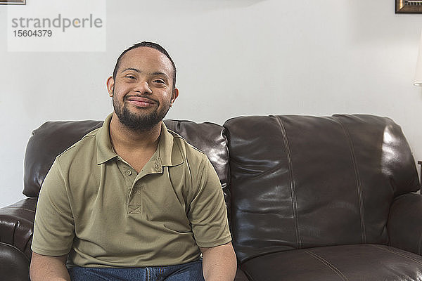 Porträt eines glücklichen afroamerikanischen Mannes mit Down-Syndrom  der zu Hause auf der Couch sitzt