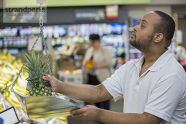Mann mit Down-Syndrom beim Wiegen von Ananas in einem Lebensmittelladen