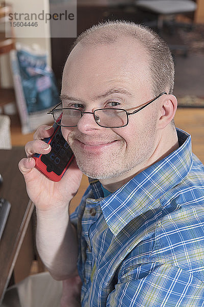 Mann mit Down-Syndrom telefoniert mit seinem Handy während der Arbeit in einem Büro