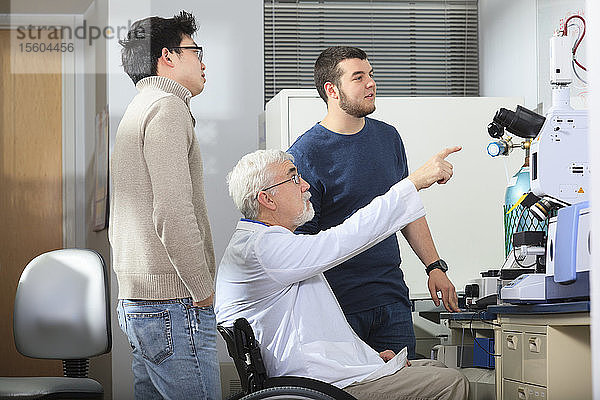 Professor mit Muskeldystrophie arbeitet mit Studenten der Ingenieurwissenschaften an einem Röntgenfluoreszenzanalysegerät in einem Labor