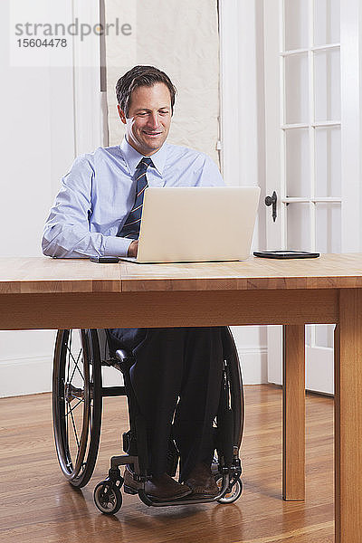 Geschäftsmann mit Querschnittslähmung im Rollstuhl bei der Arbeit am Laptop