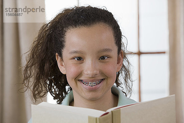 Porträt eines hispanischen Mädchens  das ein Buch liest und lächelt