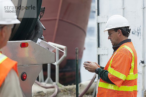 Umweltingenieur  der auf einem Schiff im Hafen eine SMS auf seinem Handy schreibt