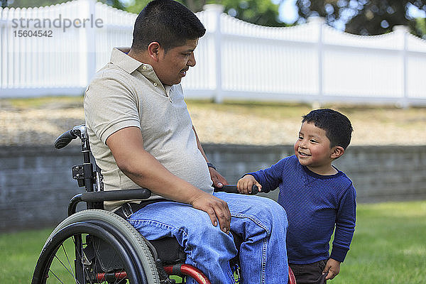 Hispanischer Mann mit Rückenmarksverletzung im Rollstuhl mit seinem Sohn auf dem Rasen