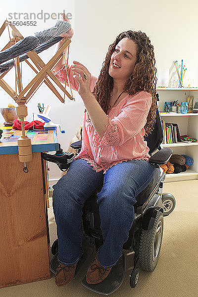 Frau mit Muskeldystrophie bei der Arbeit mit ihrem Regenschirmfadenwickler auf ihrem elektrischen Stuhl