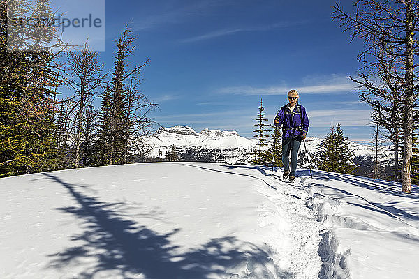 Wanderin auf schneebedecktem Weg mit schneebedeckten Bergen  blauem Himmel und Wolken im Hintergrund; Lake Louise  Alberta  Kanada
