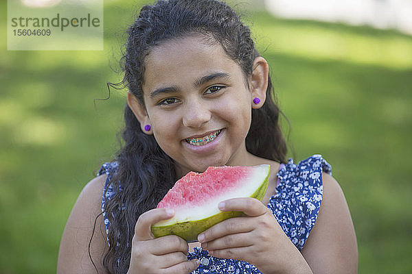Porträt eines glücklichen hispanischen Teenagers  der eine Wassermelone mit Zahnspange isst
