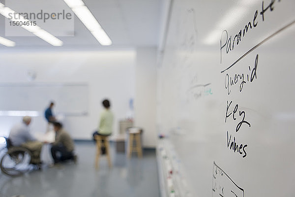 Text auf einem Whiteboard in einem Klassenzimmer mit einem Professor mit Muskeldystrophie im Hintergrund