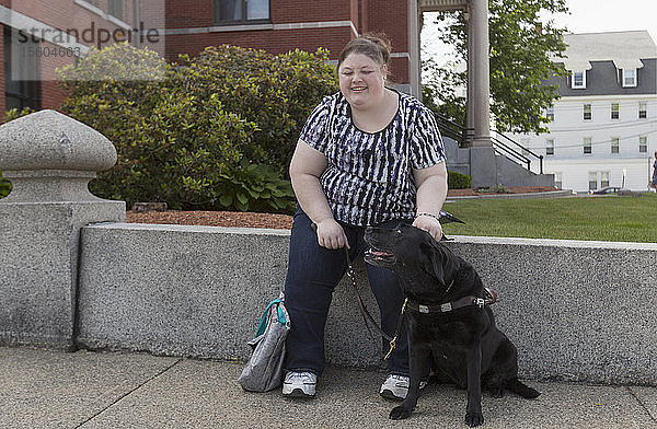 Frau mit Sehbehinderung sitzt mit ihrem Diensthund auf einem Bordstein