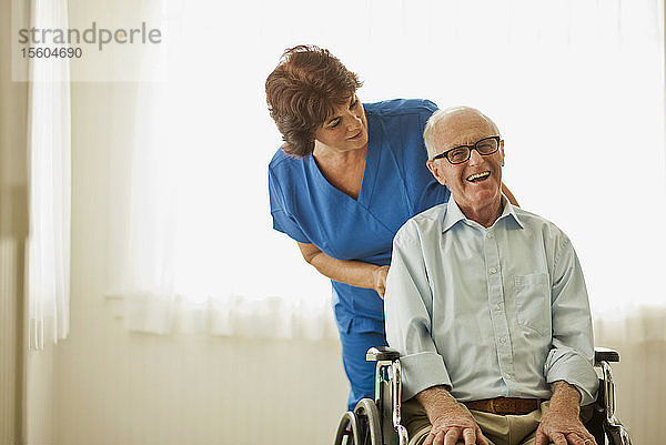 Porträt eines lächelnden älteren Mannes  der von einer Krankenschwester getröstet wird  während er in einem Rollstuhl sitzt