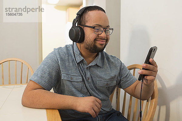 Glücklicher afroamerikanischer Mann mit Down-Syndrom  der zu Hause mit Kopfhörern am Telefon Musik hört