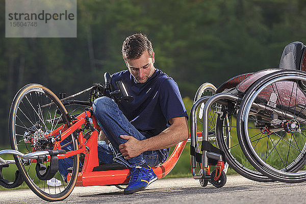 Ein Mann mit einer Rückenmarksverletzung in seinem speziell angefertigten adaptiven Handbike beim Einsteigen in seinen Rollstuhl