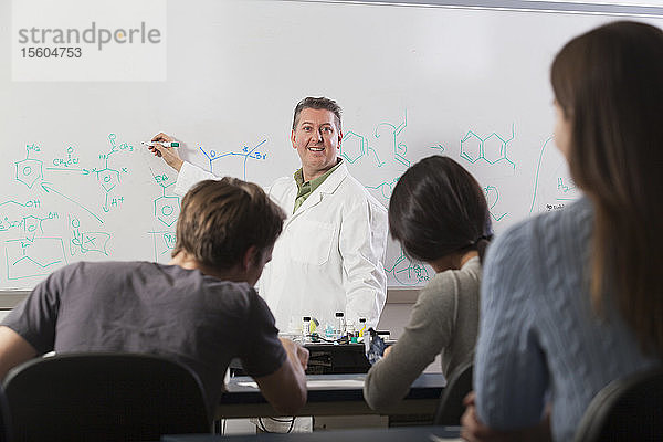 Studenten sitzen in einem technischen Klassenzimmer und hören einem Professor zu  der über chemische Benzolringbindungen spricht