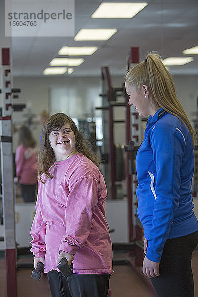 Junge Frau mit Down-Syndrom trainiert mit ihrem Trainer mit Gewichten im Fitnessstudio