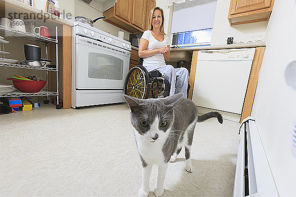 Frau mit Querschnittslähmung in ihrer begehbaren Küche  die eine Katze betrachtet