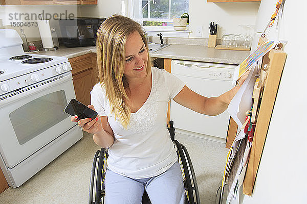 Frau mit Querschnittslähmung in ihrer barrierefreien Küche  die auf eine Tafel schaut