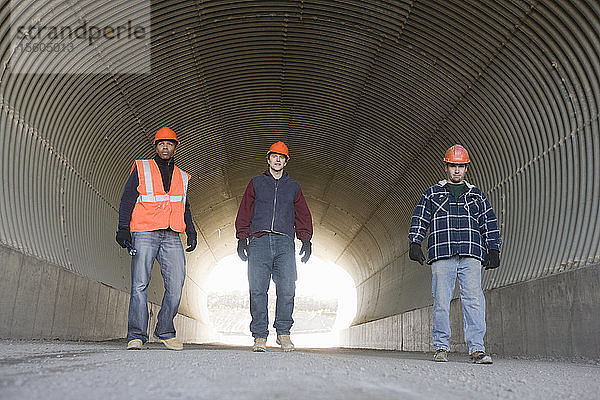 Drei Ingenieure gehen in einem Tunnel in einem Asphaltwerk