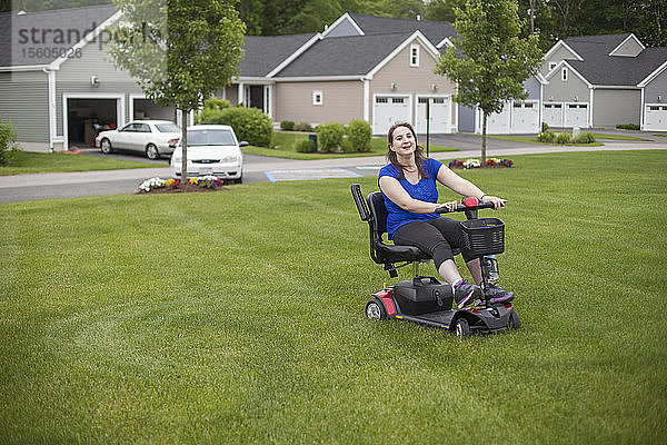 Junge Frau mit zerebraler Lähmung fährt mit ihrem Motorroller auf ihrem Rasen