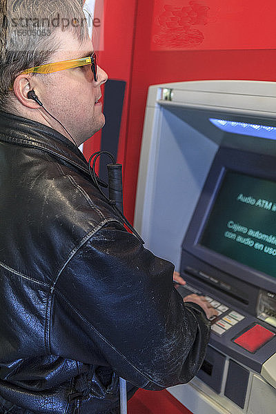 Ein Mann mit angeborener Blindheit benutzt einen Geldautomaten