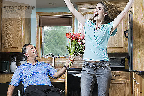 Mittlerer erwachsener Mann im Rollstuhl schenkt einer lachenden mittleren erwachsenen Frau Blumen