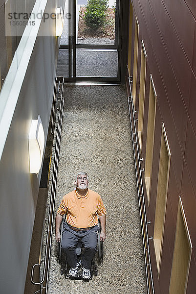 Blick von oben auf einen Mann mittleren Alters mit Muskeldystrophie  der in einem Rollstuhl in einer Bibliothek sitzt