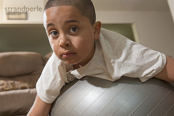 Hispanischer Junge mit Autismus spielt mit einem Gymnastikball im Wohnzimmer