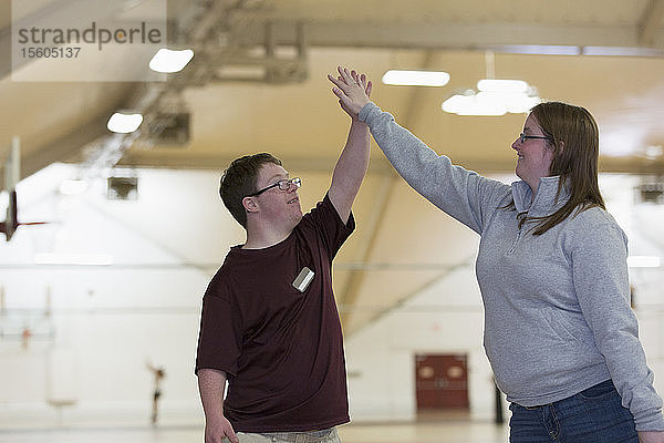 Junger Mann mit Down-Syndrom macht High-Five mit einem Schüler in der Turnhalle