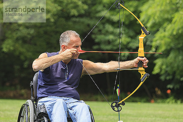 Mann mit Rückenmarksverletzung im Rollstuhl zielt mit Pfeil und Bogen zum Bogenschießen