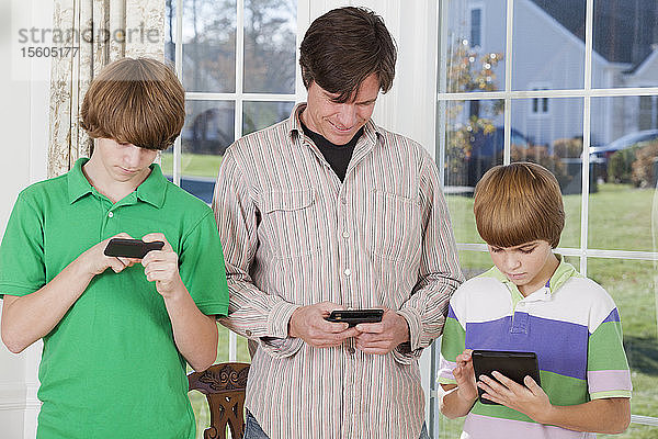 Mann und seine beiden Söhne benutzen Smartphones und ein digitales Tablet