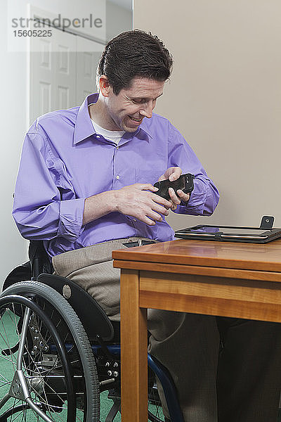 Mann im Rollstuhl mit Rückenmarksverletzung hat Probleme mit der Handgeschicklichkeit bei der Benutzung seines Mobiltelefons