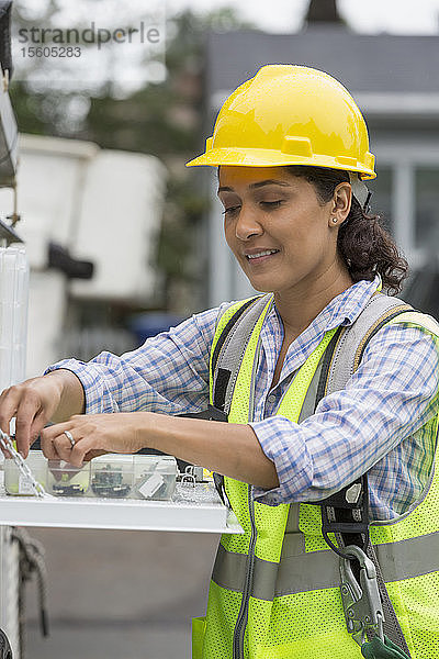 Hispanische Mitarbeiterin eines Versorgungsunternehmens mit einer Kiste mit Kabelverstärkern auf einer Baustelle